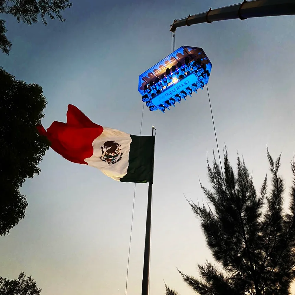 Mesa de Dinner in the Sky suspendida junto a la bandera de México, al atardecer